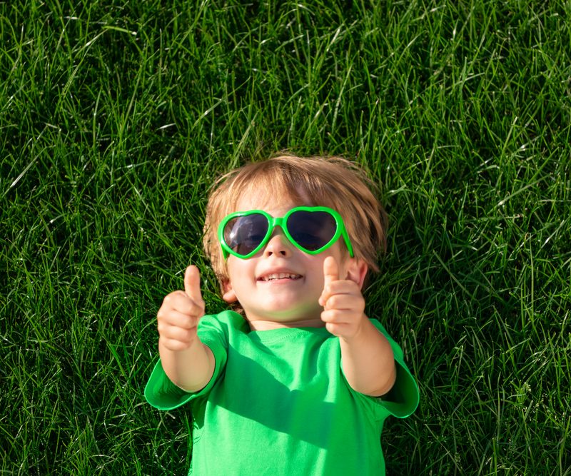 Happy child laying on green grass giving thumbs up