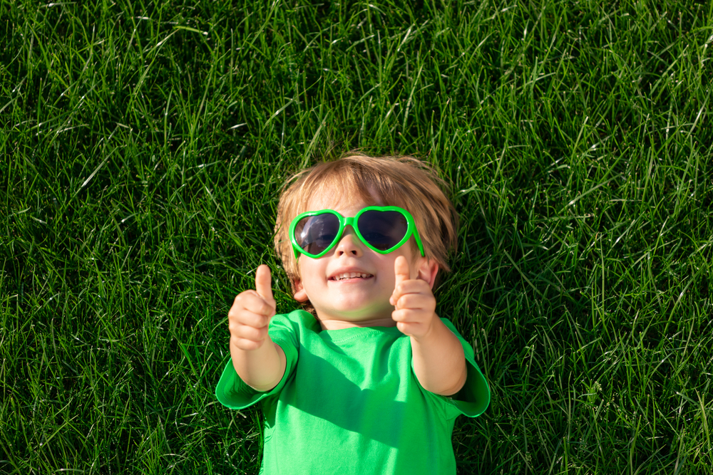 Happy child laying on green grass giving thumbs up
