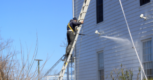 Man on tall ladder washing a house